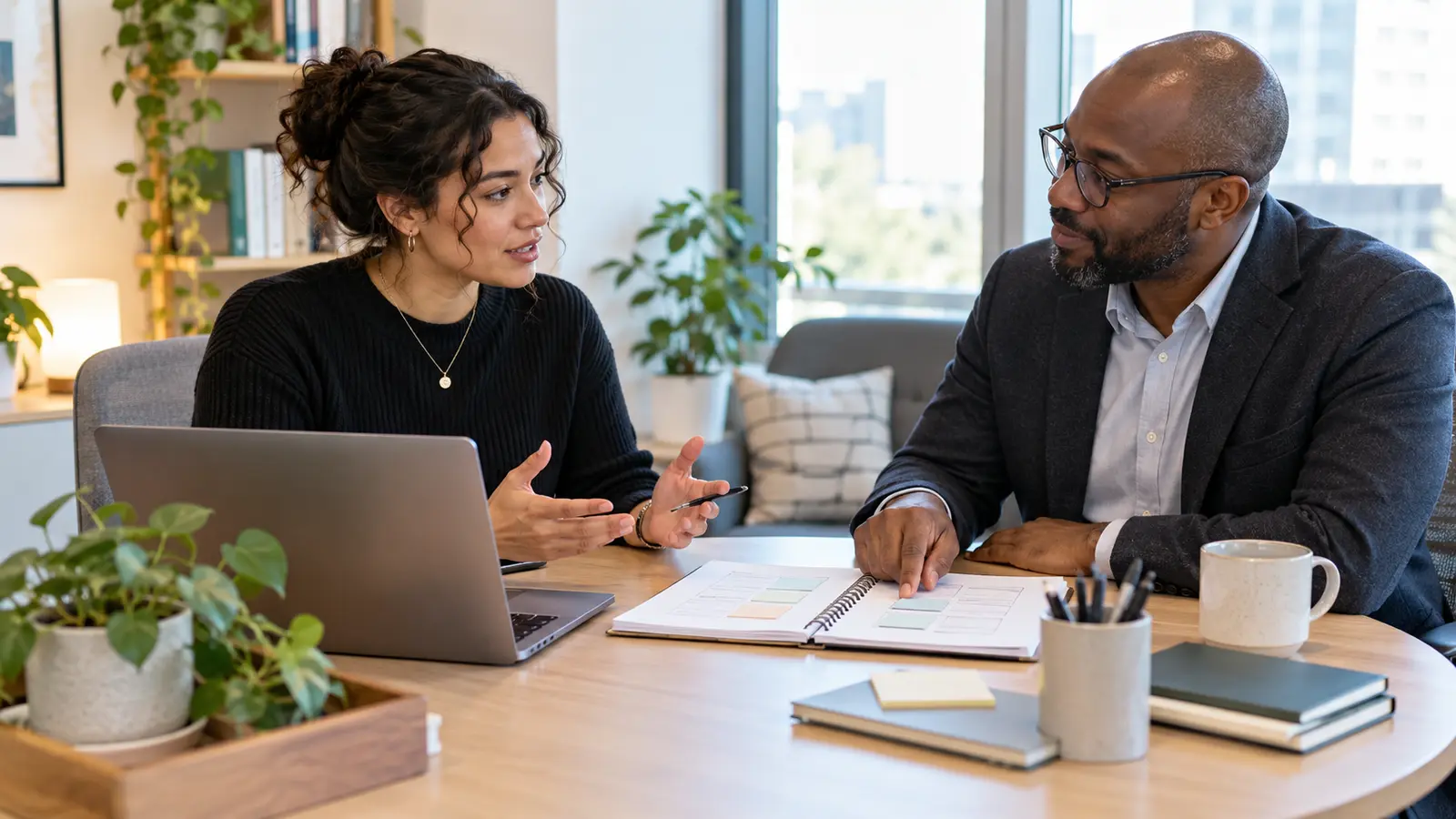 An employee and manager have a calm private conversation while reviewing a practical work plan in a bright office